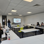 A person presents on sustainability in the restaurant sector to a small audience in a modern classroom with laptops and a projector.