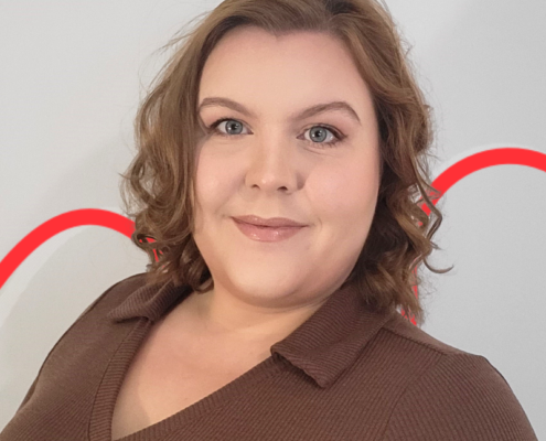 A person with shoulder-length hair smiles at the camera against a plain background with a red curved line.