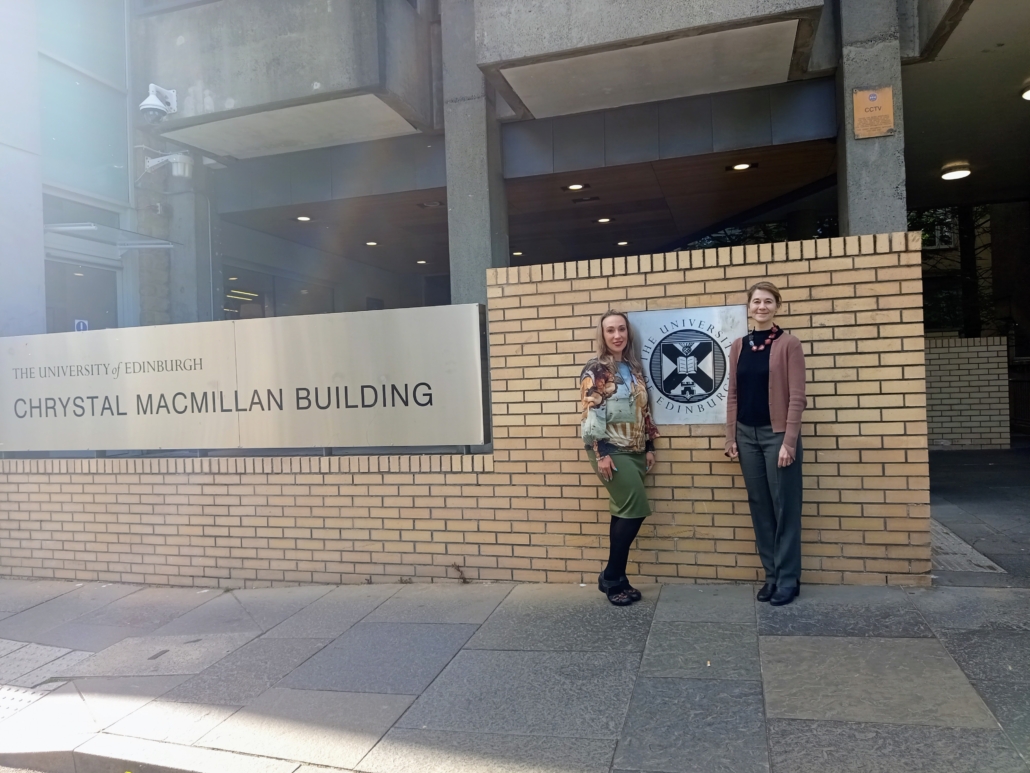 Two people stand outside the University of Edinburgh's Chrystal Macmillan Building, near a prominent university sign.