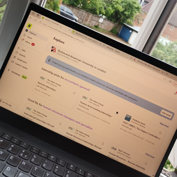 A laptop displays a university internship webpage in a home setting with a garden view through the window in the background.