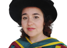 A person in academic regalia, with a black hat and colorful robes, poses against a plain white background, suggesting a graduation ceremony.
