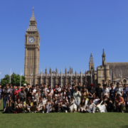 A group of people pose in front of Big Ben and the Houses of Parliament on a sunny day in London.