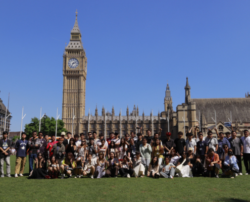 A group of people pose in front of Big Ben and the Houses of Parliament on a sunny day in London.