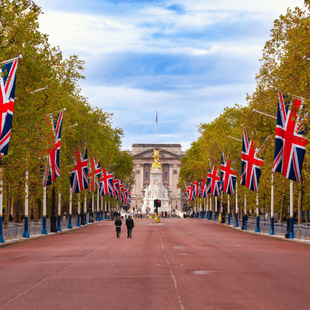The image shows The Mall leading to Buckingham Palace decorated with Union flags, featuring trees and two people walking toward the Victoria Memorial.