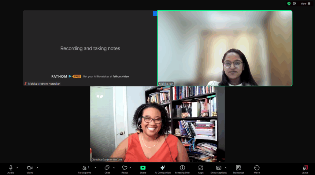 Two people on a video call. One person smiles, seated near a bookshelf. The other person has a neutral expression.