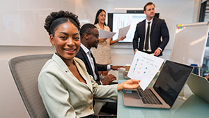 A group of four people in a modern office setting, engaged in a business presentation with charts and laptops.