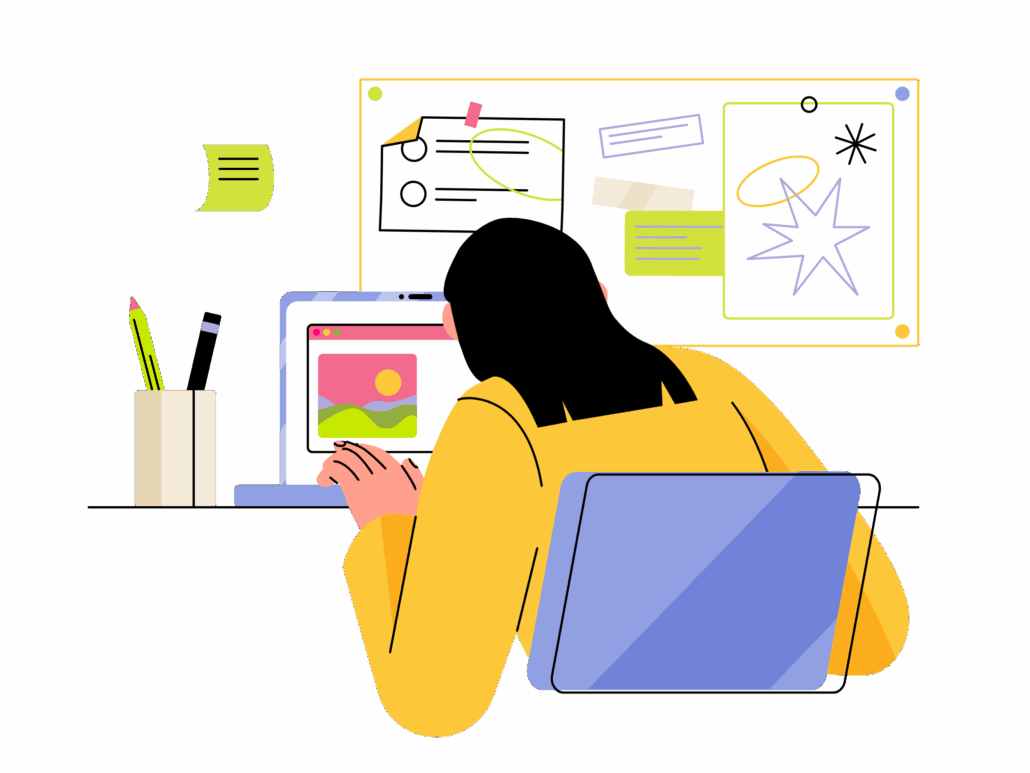 A person working on a laptop at a desk with a pencil holder, notes, and colorful images on a whiteboard.