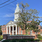 Mercy University A historical building with a white clock tower and columns surrounded by trees, at Georgia College & State University on a sunny day.