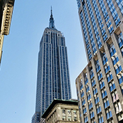 newyork The image shows the Empire State Building in New York City, surrounded by other skyscrapers, under a clear blue sky.