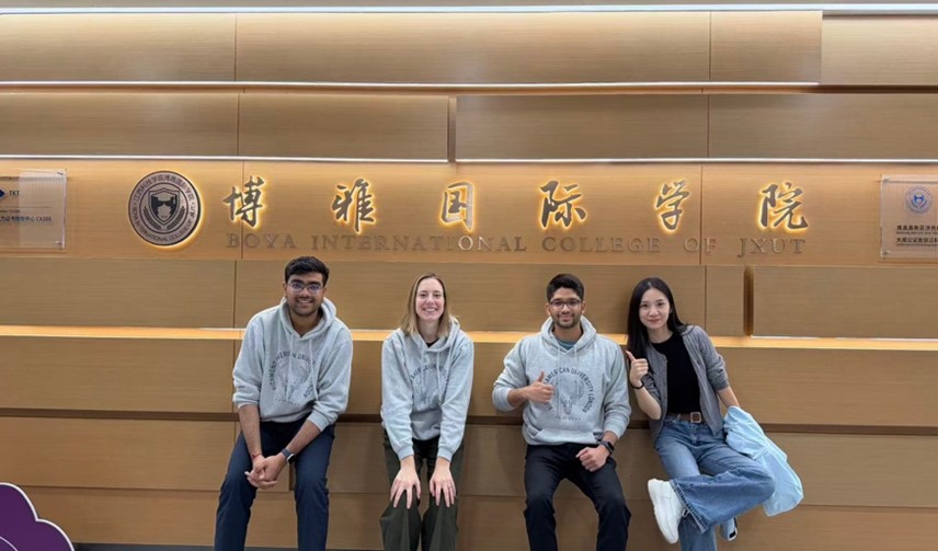 Four people sit in front of a sign for Boya International College of JXUT, smiling and casually dressed in a hallway.