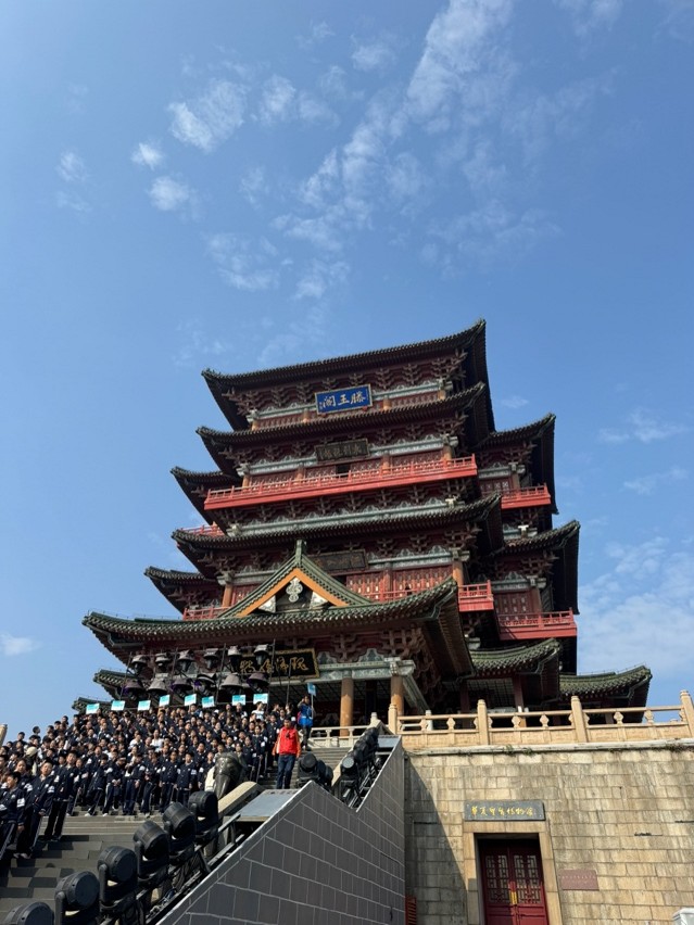 A group gathers in front of the ancient Pavilion of Prince Teng, a historic multi-tiered structure under a clear blue sky.
