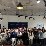 A group of people gather and pose indoors at Richmond American University London, with casual attire under modern ceiling lights.
