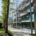 A modern building with glass windows stands beside a tree-lined path. People walk near bike racks on a sunny day.