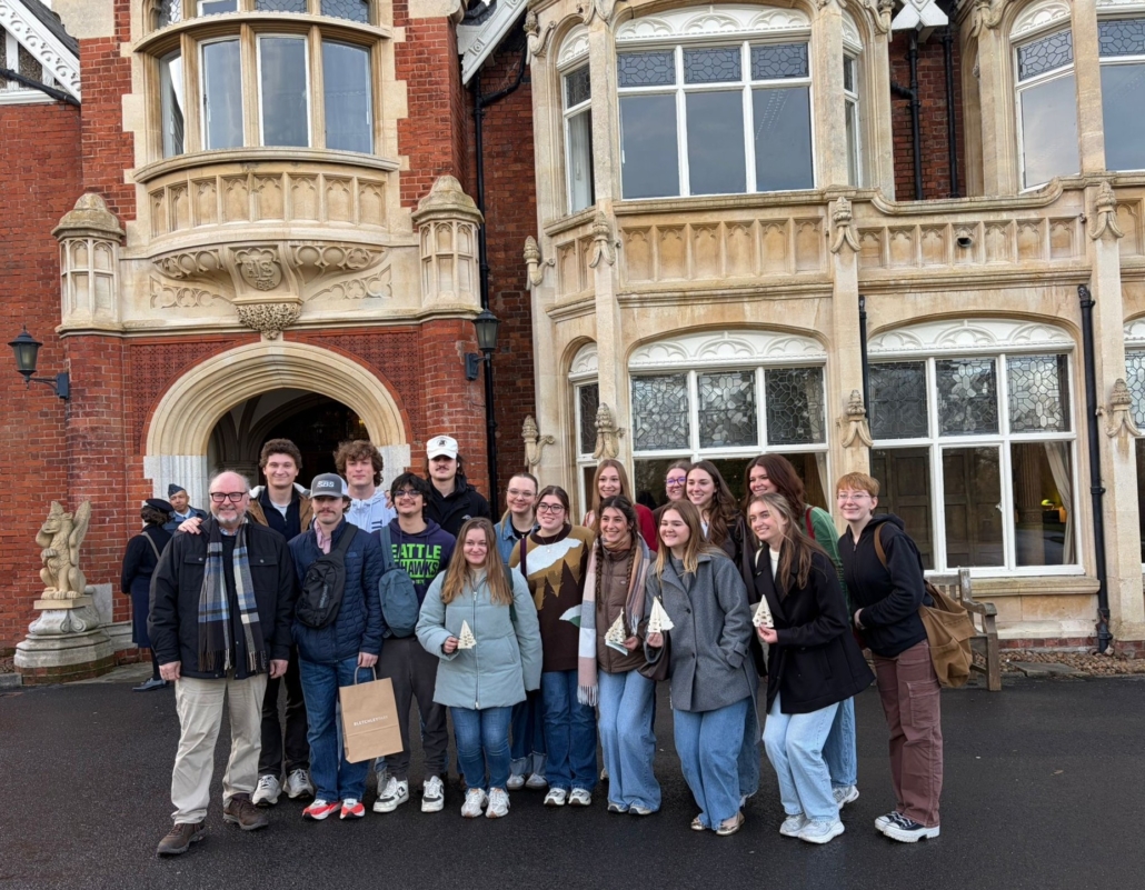A group poses outside Bletchley Park, a historic site in England, with ornate architecture and large windows.